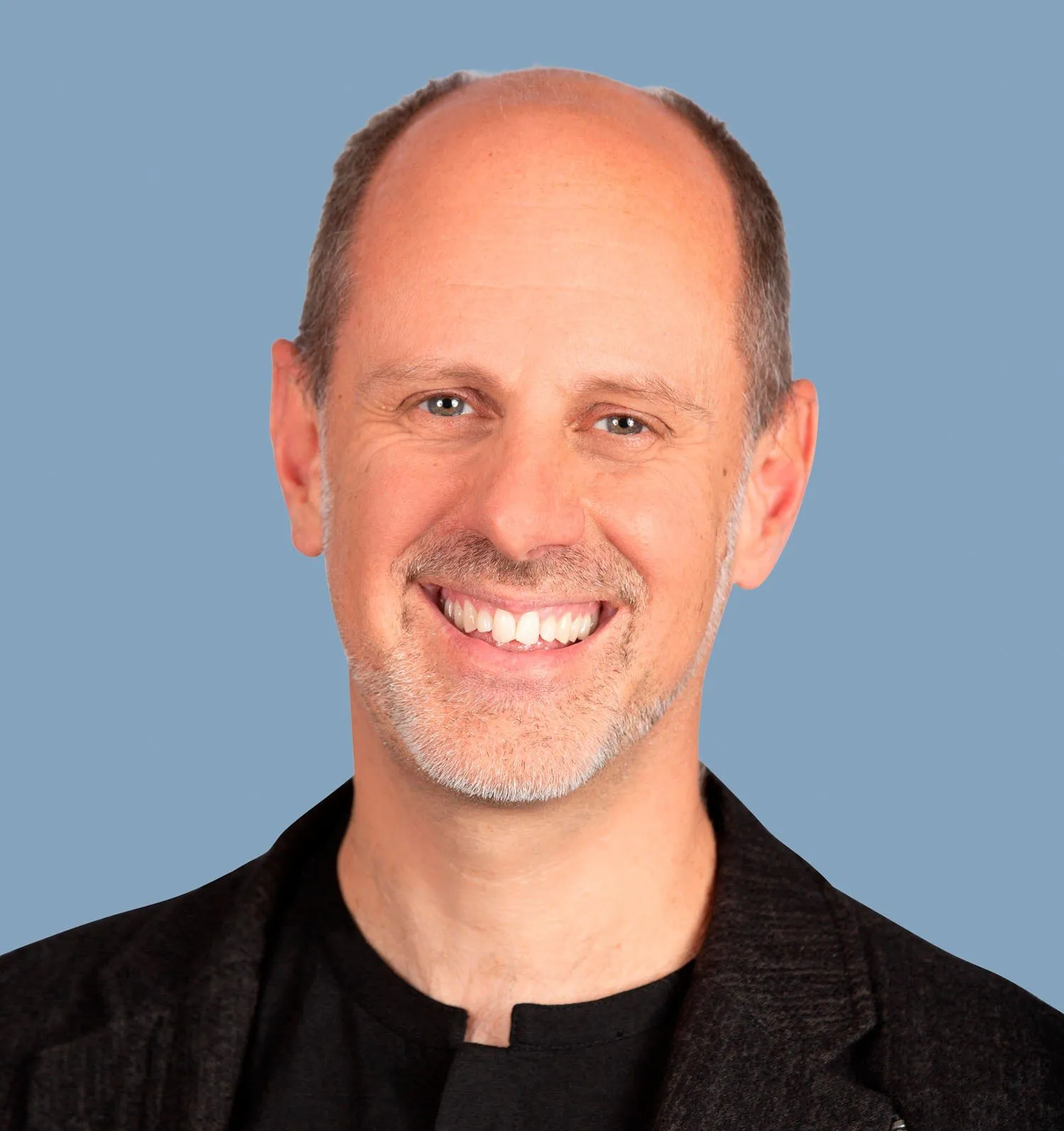Portrait de Mike Haley, SVP recherche d'Autodesk, souriant, en veste sombre, sur fond bleu uni.