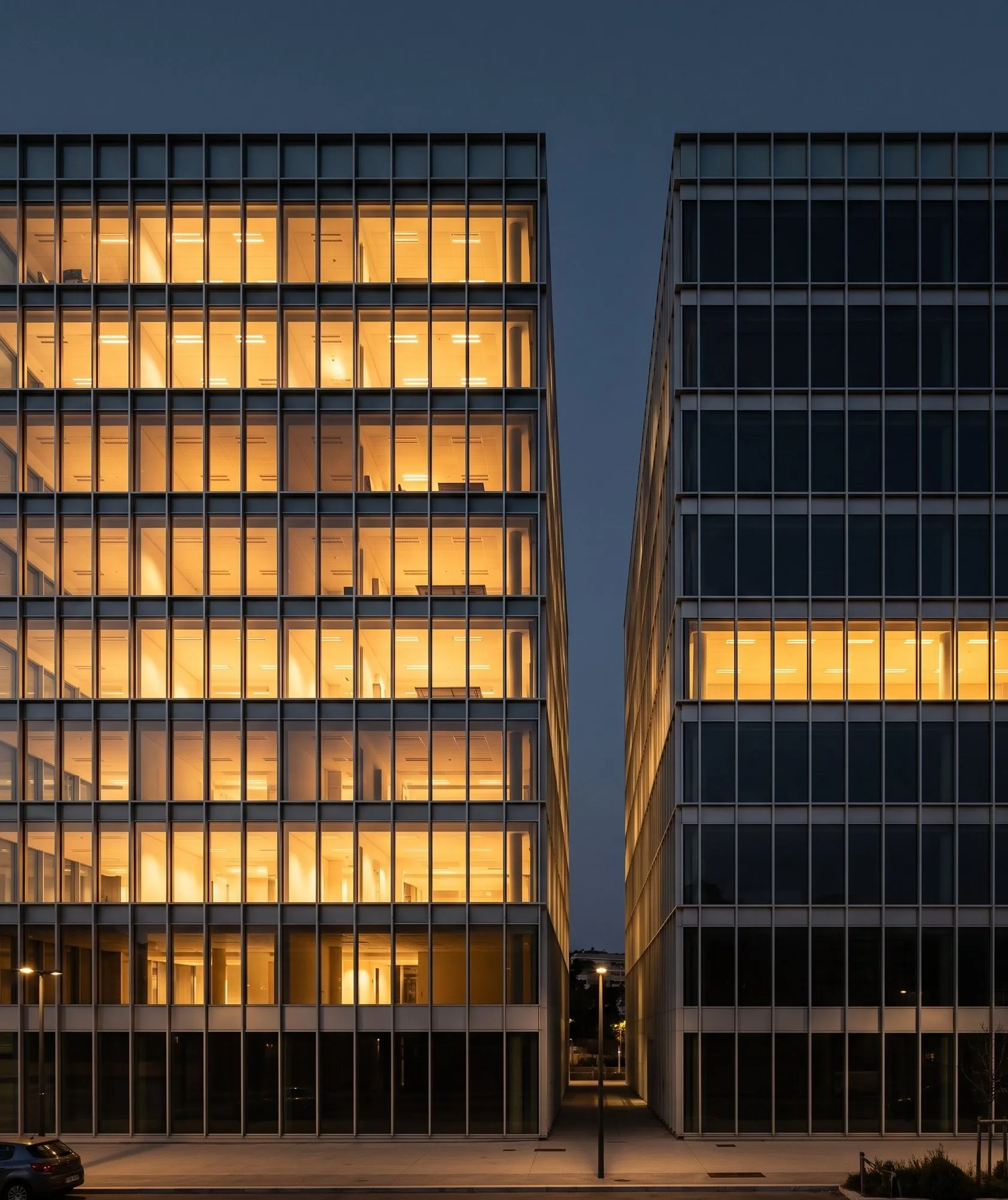 Deux façades d’immeubles de bureaux au crépuscule : celle de gauche entièrement éclairée de l’intérieur, celle de droite presque éteinte à l’exception d’un seul niveau.